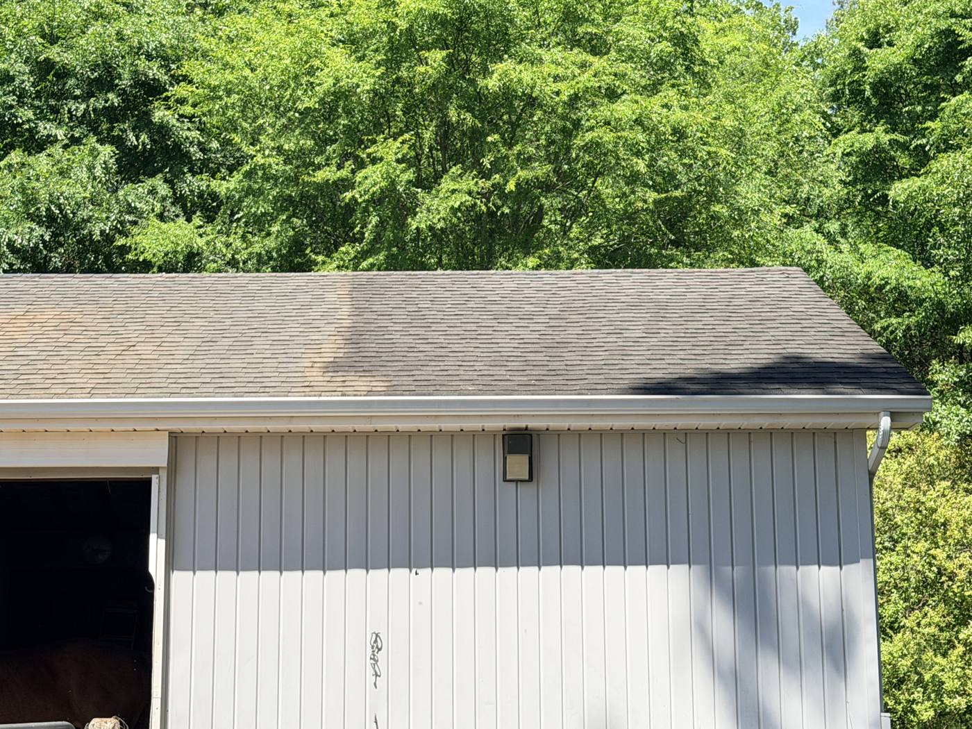 Roof partway through a soft wash, half clean and half still streaked with algae